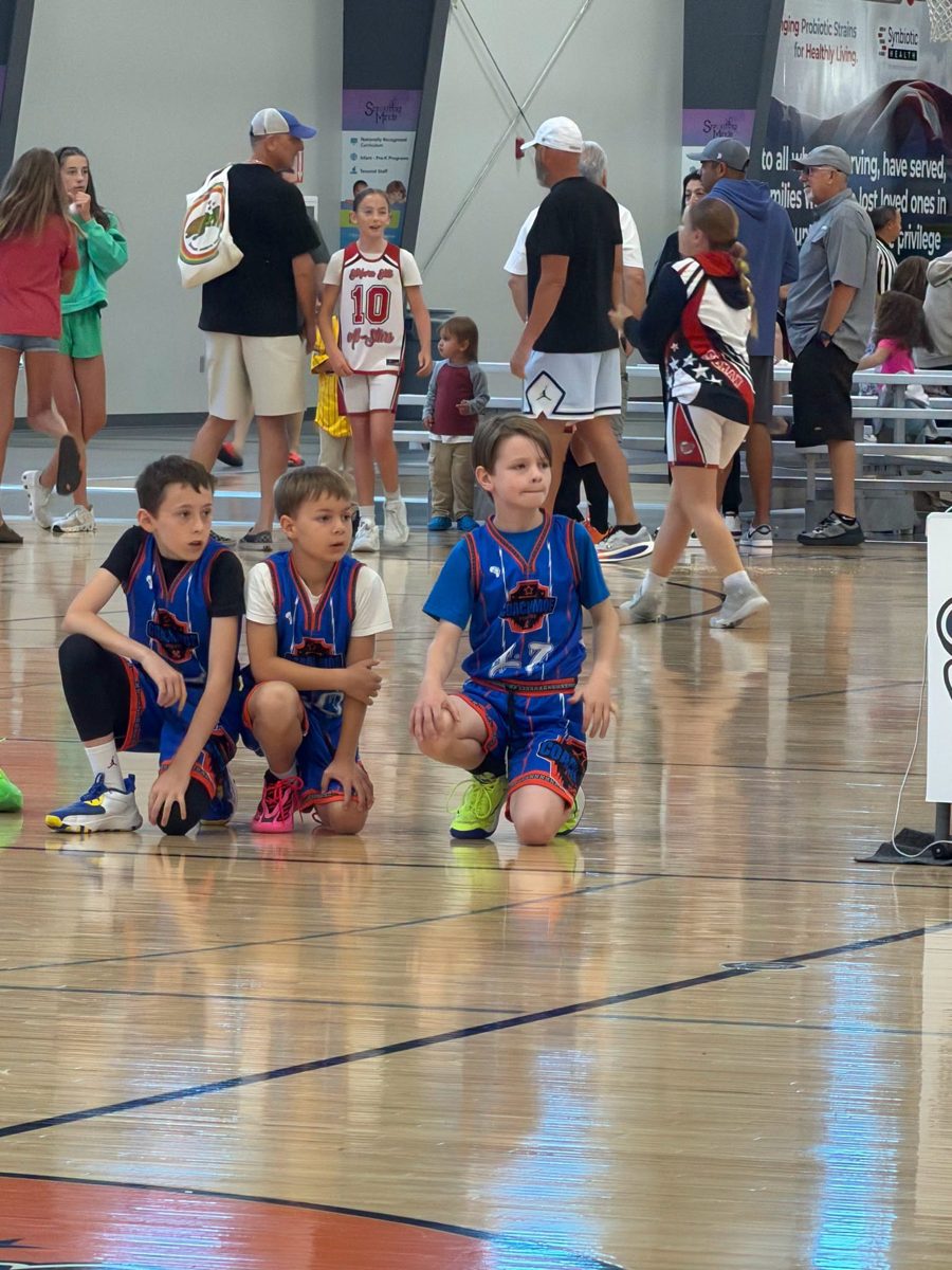 Young CMA players in team jerseys kneeling courtside at a tournament